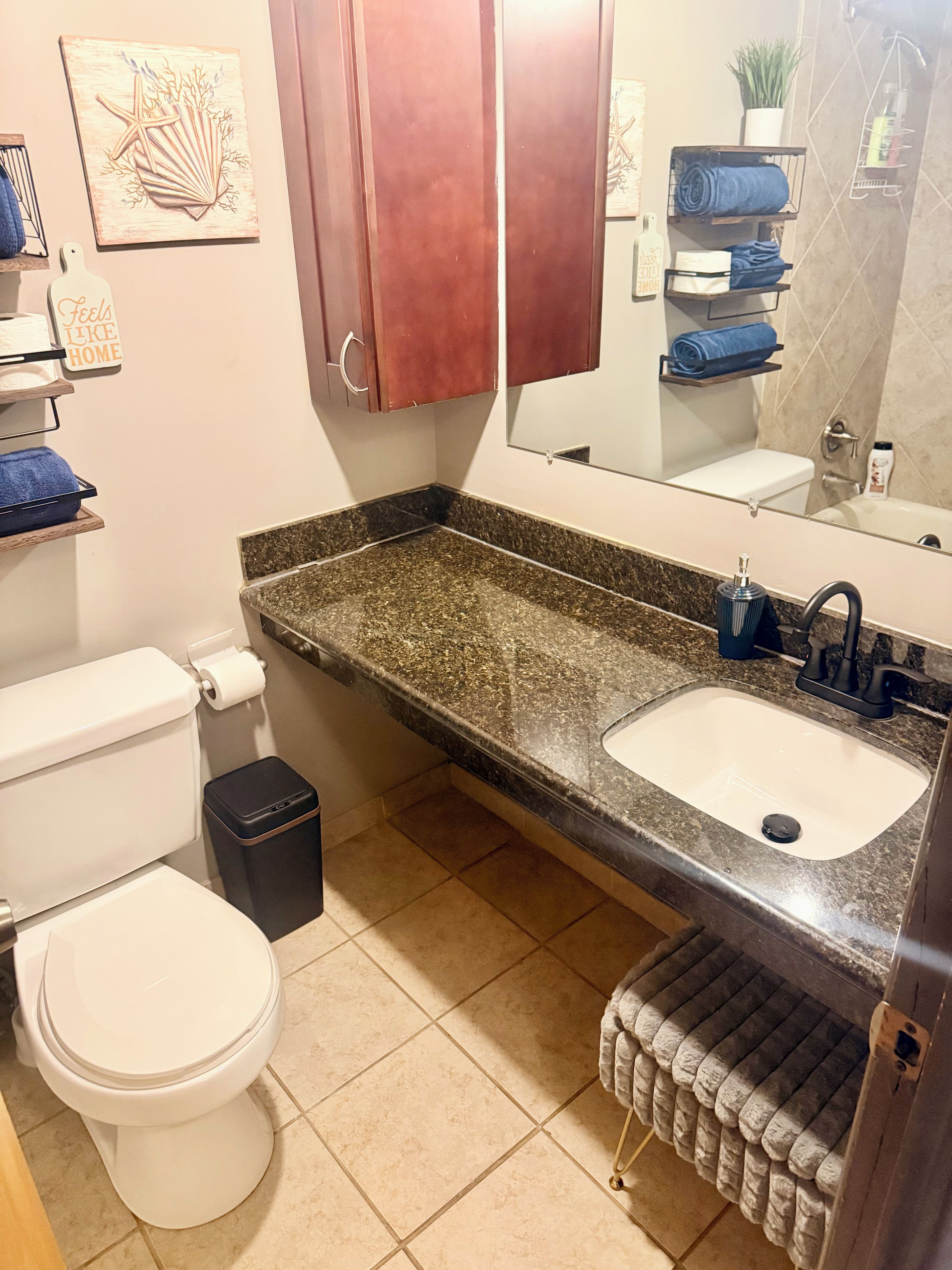 Ein Badezimmer mit Toilette, Waschbecken und Spiegel. Handtücher und ein Mülleimer befinden sich an einem Handtuchhalter.