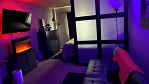 Een moderne woonkamer met een flatscreen-televisie, een open haard, een bank en een groot raam met zonwering.
