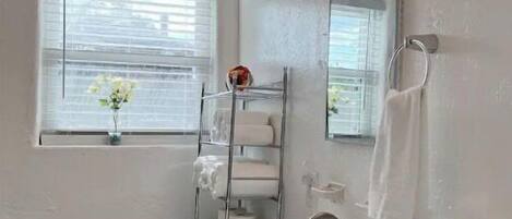 A modern bathroom with a toilet, sink, and mirror. There is a window with blinds and a towel rack.