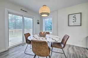Un coin repas avec une table ronde, quatre chaises marron, un lustre et une œuvre d’art encadrée accrochée au mur.