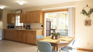 Una cocina con armarios de madera, una mesa de comedor con sillas y vistas al exterior a través de una puerta corrediza de vidrio.