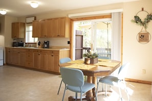 Une cuisine avec des meubles en bois, une table à manger avec des chaises, et une vue sur l’extérieur grâce à une porte-fenêtre coulissante.