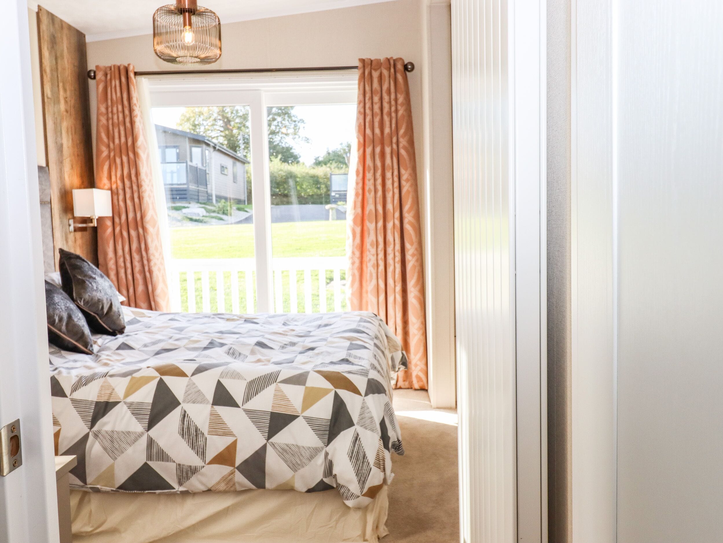 A bedroom with a bed, pillows, a lamp, and a view of a house and lawn through a window.