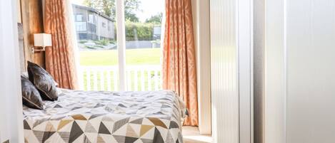 A bedroom with a bed, pillows, a lamp, and a view of a house and lawn through a window.