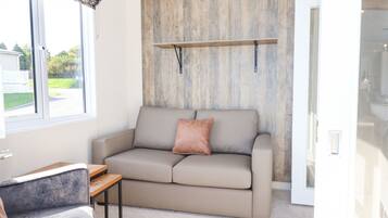 Una sala de estar moderna con un sofá color beige, una mesita de madera y un ventanal con vistas a una casa y vegetación.