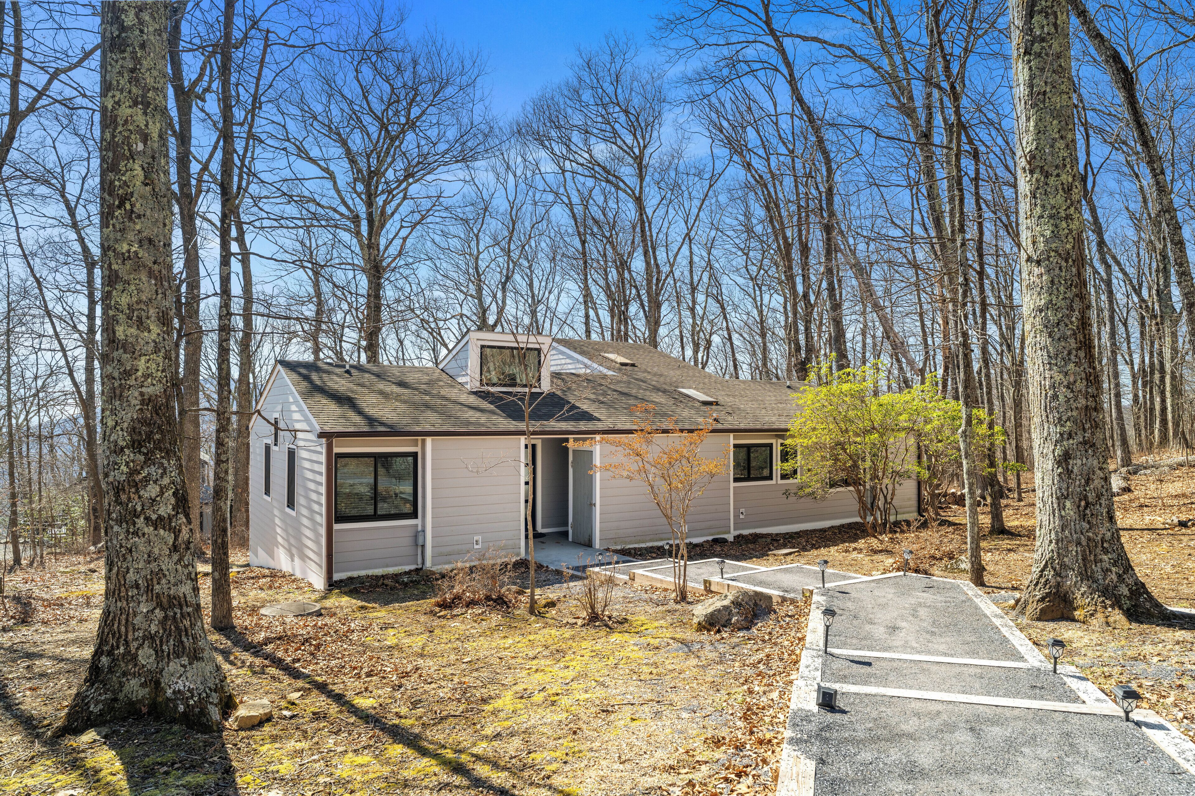 A small cabin with a sloped roof, surrounded by trees, and a paved driveway leading to the entrance.