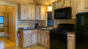 A wooden cabin kitchen with built-in cabinets, a stove, a microwave, and a refrigerator.