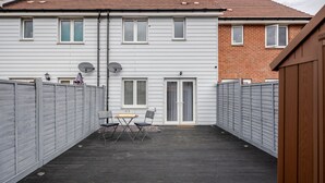 A covered patio with a table and chairs, surrounded by a wooden fence.