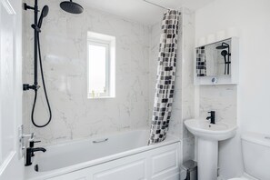A modern bathroom with a white bathtub, a showerhead, a sink, and a toilet. - Lovely 2-bed House With 2 Bathrooms in Dartford (Dartford)