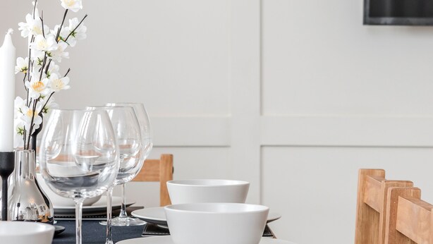 A dining table set with white plates, bowls, and wine glasses, accompanied by a candle and flowers.