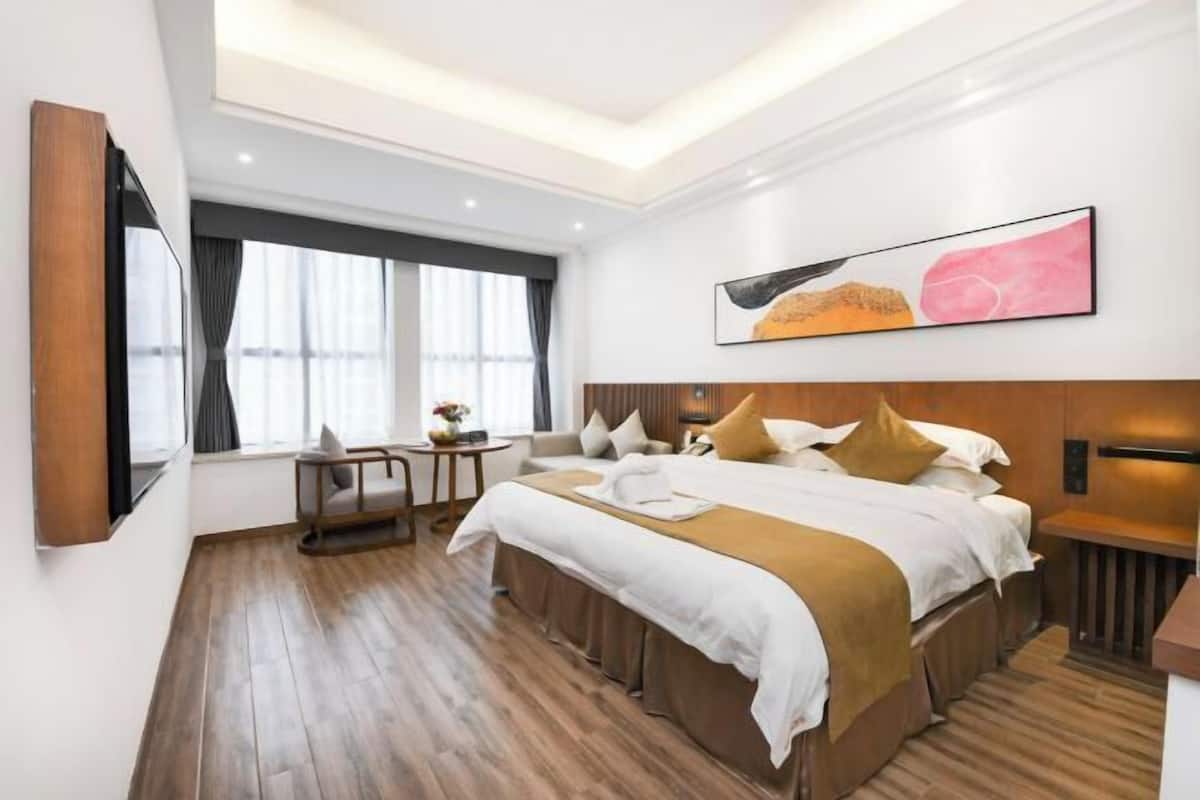 A modern hotel room with a large bed, a desk, a chair, and a large window.