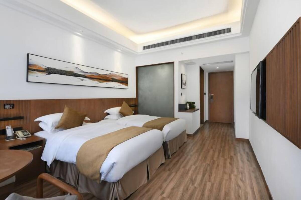 A hotel room with two beds, a desk, a chair, a telephone, and a painting on the wall.