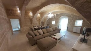 Un loft spacieux doté d’un plafond voûté en pierre, d’un grand canapé d’angle, d’une table à manger avec des chaises et d’un meuble blanc.