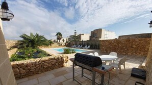 Une terrasse avec un barbecue, des sièges d’extérieur, une piscine et des murs en pierre.