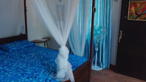 Una cama con dosel, un ventilador de pie y una puerta con una pintura colorida.