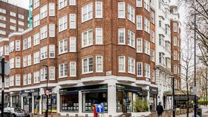 A multi-story building with a brick facade and white trim, featuring a ground-level entrance with a blue sign. - ' Luxury & Spacious AirCondisioned 4 Bed 4 Bath Apartment ' (London)