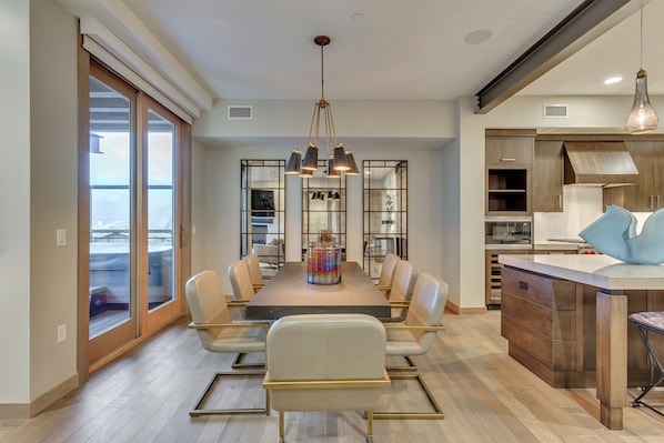 A modern dining area with a long table, chairs, and a central chandelier.