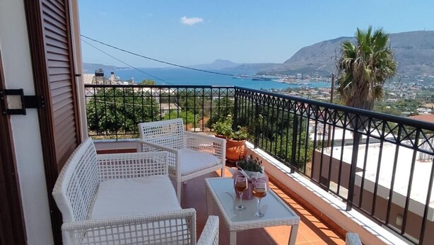 A balcony with white wicker furniture, a small table with two glasses of wine, and a view of the sea and mountains. - Chrisa's Beautiful Apartment  (Chania)