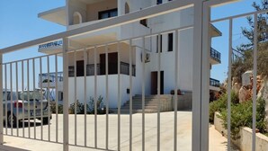 A modern two-story building with a white exterior, a balcony on the upper floor, and a gated entrance. - Chrisa's Beautiful Apartment  (Chania)