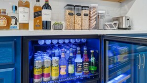Un coin cuisine équipé d’un réfrigérateur rempli de boissons et d’une étagère où sont rangées des bouteilles et des bocaux.
