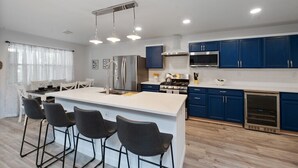 Une cuisine moderne avec des meubles bleus, un îlot central doté de tabourets de bar, des appareils en acier inoxydable et un éclairage suspendu.