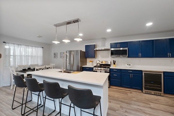 Una cocina moderna con armarios azules, una isla central con taburetes de bar, electrodomésticos de acero inoxidable e iluminación colgante.
