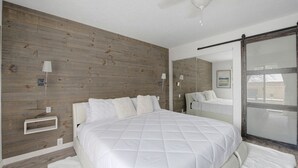 Une chambre avec un grand lit, des murs recouverts de panneaux de bois, un ventilateur de plafond et une fenêtre donnant sur un beau paysage.