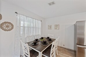 Un comedor con una mesa preparada para seis personas, sillas blancas y un refrigerador moderno de acero inoxidable.