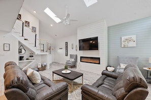 Una sala de estar moderna con sofás de cuero, chimenea, televisor y una escalera.