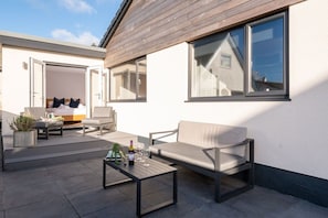 En udendørs patio med en sofa, et sofabord og en potteplante.