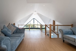 Une chambre spacieuse aménagée en loft, avec un plafond haut, un plancher en bois et une grande lucarne.