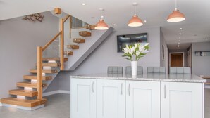 Une cuisine moderne avec un îlot central, des armoires blanches et un escalier en bois.