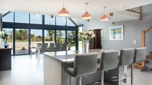 Une cuisine moderne dotée d’un grand îlot central, de tabourets de bar, de luminaires suspendus et offrant une vue sur l’extérieur.