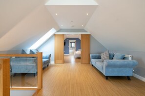 A spacious attic room with a sloped ceiling, a wooden floor, and a blue sofa. - Ty Rhos Newydd: Stunning pet-friendly, family retreat on Anglesey (Llanerch-y-medd)