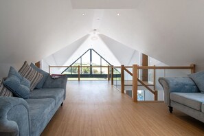 A spacious loft bedroom with a high ceiling, a wooden staircase, and a large window offering a view of the outdoors.