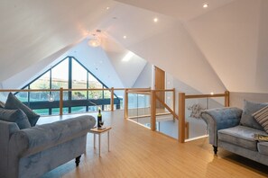 A spacious loft with a high ceiling, large windows, and a wooden staircase. - Ty Rhos Newydd: Stunning pet-friendly, family retreat on Anglesey (Llanerch-y-medd)