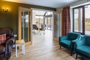 A room with a leather sofa, a teal armchair, a small wooden table, and a glass door leading to an outdoor dining area.