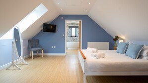 Une chambre avec un plafond en pente, un lit, une chaise, un téléviseur et une vue sur la salle de bain.