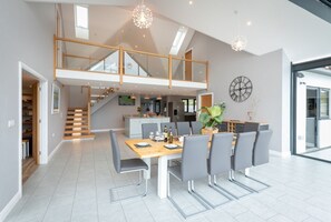 En rummelig spiseplads med højt til loftet, en trappe op til en etage, og et moderne køkken i baggrunden.