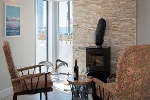 Una habitación con chimenea, dos sillones, una mesa con una botella y vasos, y un cartel en la pared.