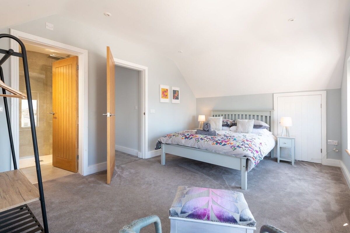 Une chambre à coucher comprenant un lit, des tables de chevet, une chaise et une porte donnant sur une autre pièce.