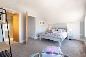 Un dormitorio con cama, mesitas de noche, una silla y una puerta que da a otra habitación.