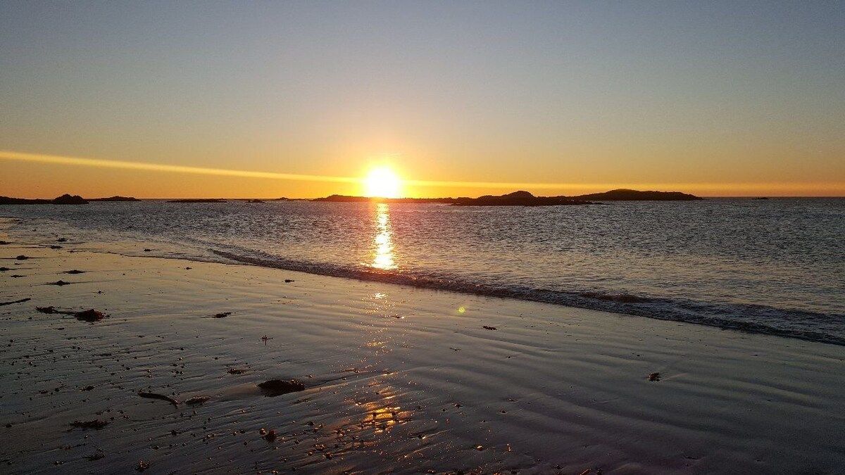 Une plage où le soleil se couche sur l’eau, créant une surface calme et propice à la contemplation.