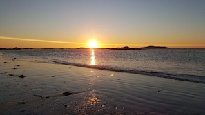 Una playa con el sol poniéndose sobre el agua, creando una superficie tranquila y serena.