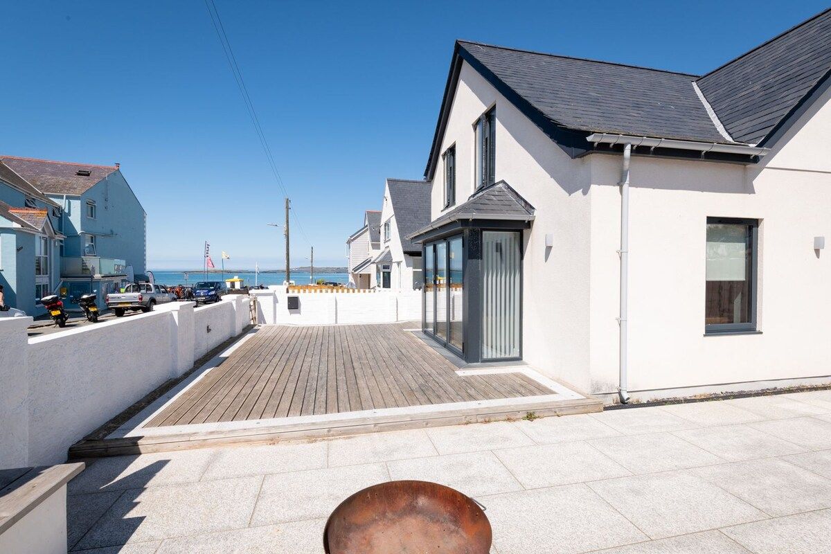 Un quartier résidentiel en bord de mer, avec une terrasse en bois, des maisons blanches et une vue dégagée sur la mer.