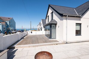 Una zona residencial costera con una terraza de madera, casas blancas y una vista despejada del mar.