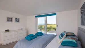 Een slaapkamer met een groot bed, een dressoir en uitzicht op zee.