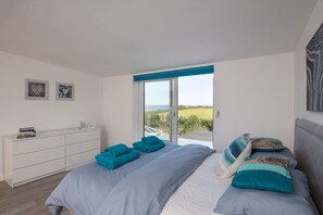A bedroom with a bed, a white dresser, and a view of the outdoors through a glass door.