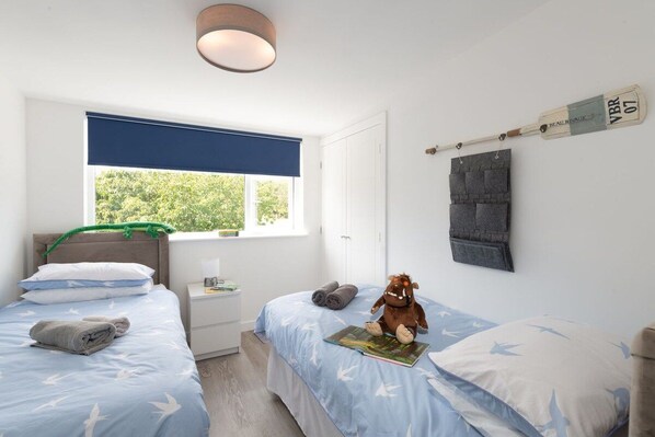 A bedroom with two beds, a window with a view, a wall-mounted cricket bat, and a stuffed toy.
