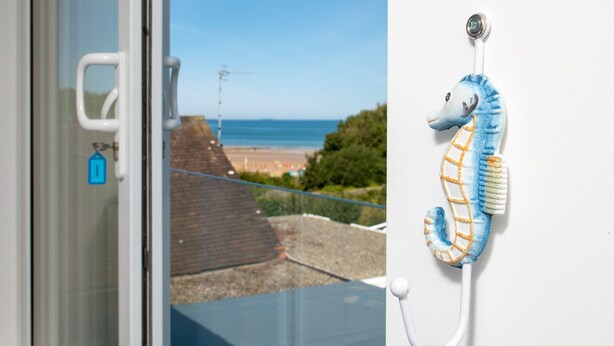 Een raam met uitzicht op een strand en een zeepaarddecoratie aan de muur.